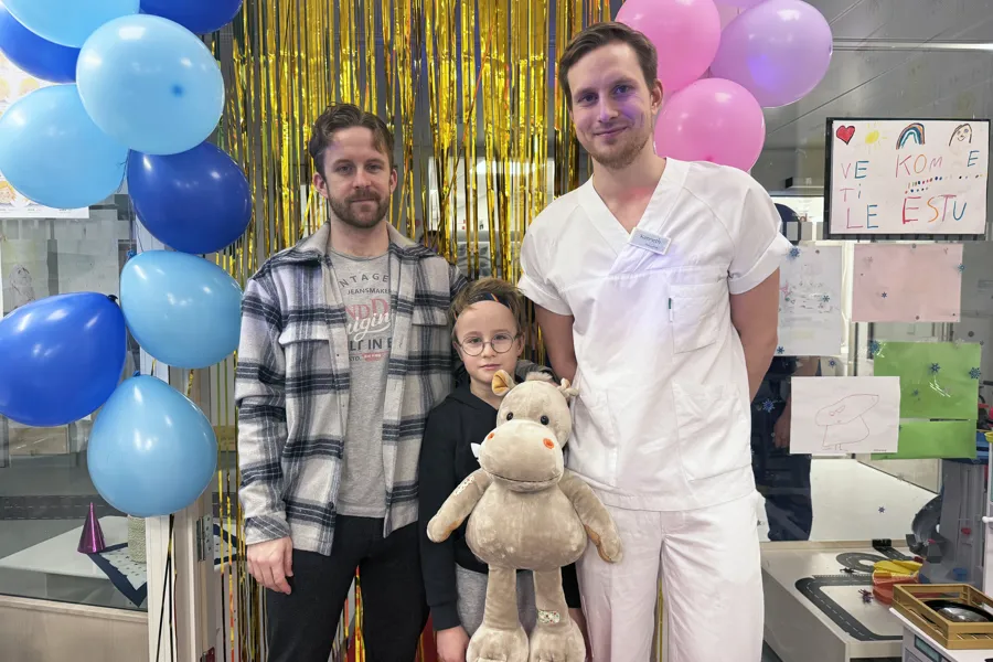 Tre personer og en bamse står samlet og smiler