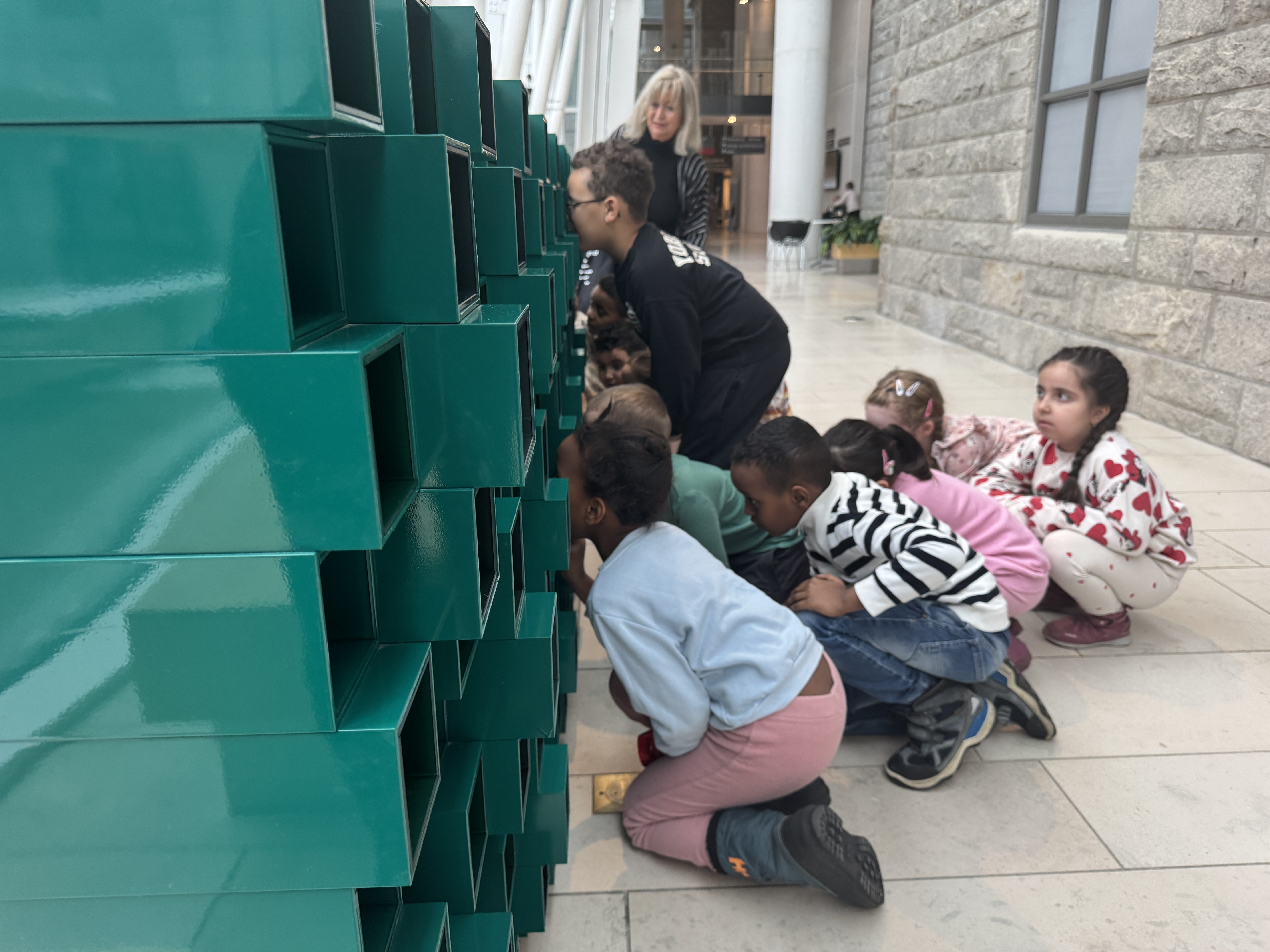 En gruppe barn som sitter på bakken ved siden av en grønn skulptur