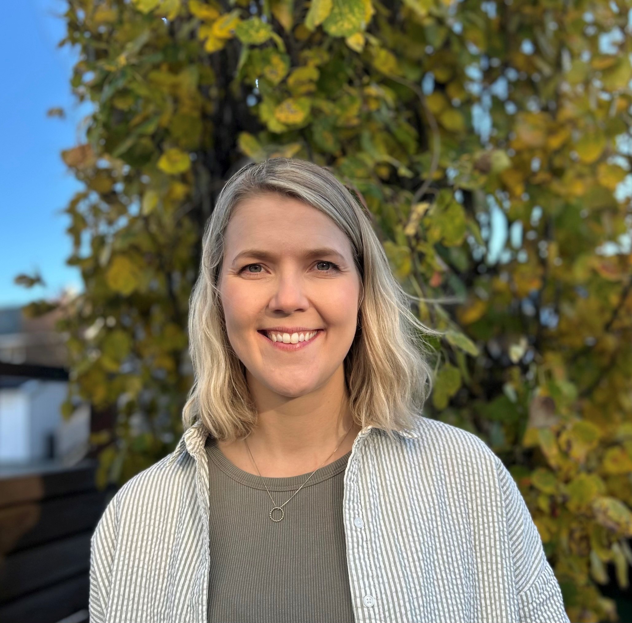 En person som smiler foran et tre