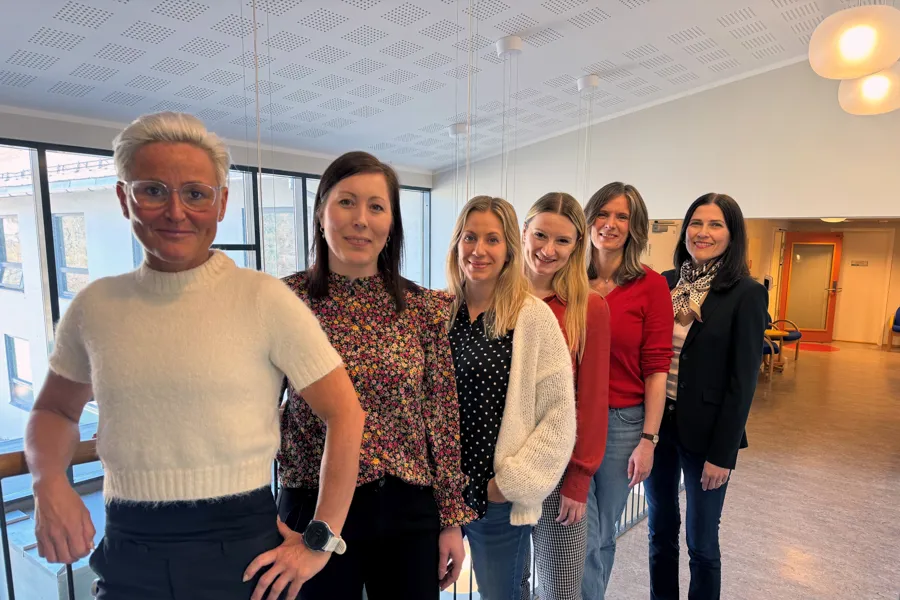 Seks damer står på rekke og smiler