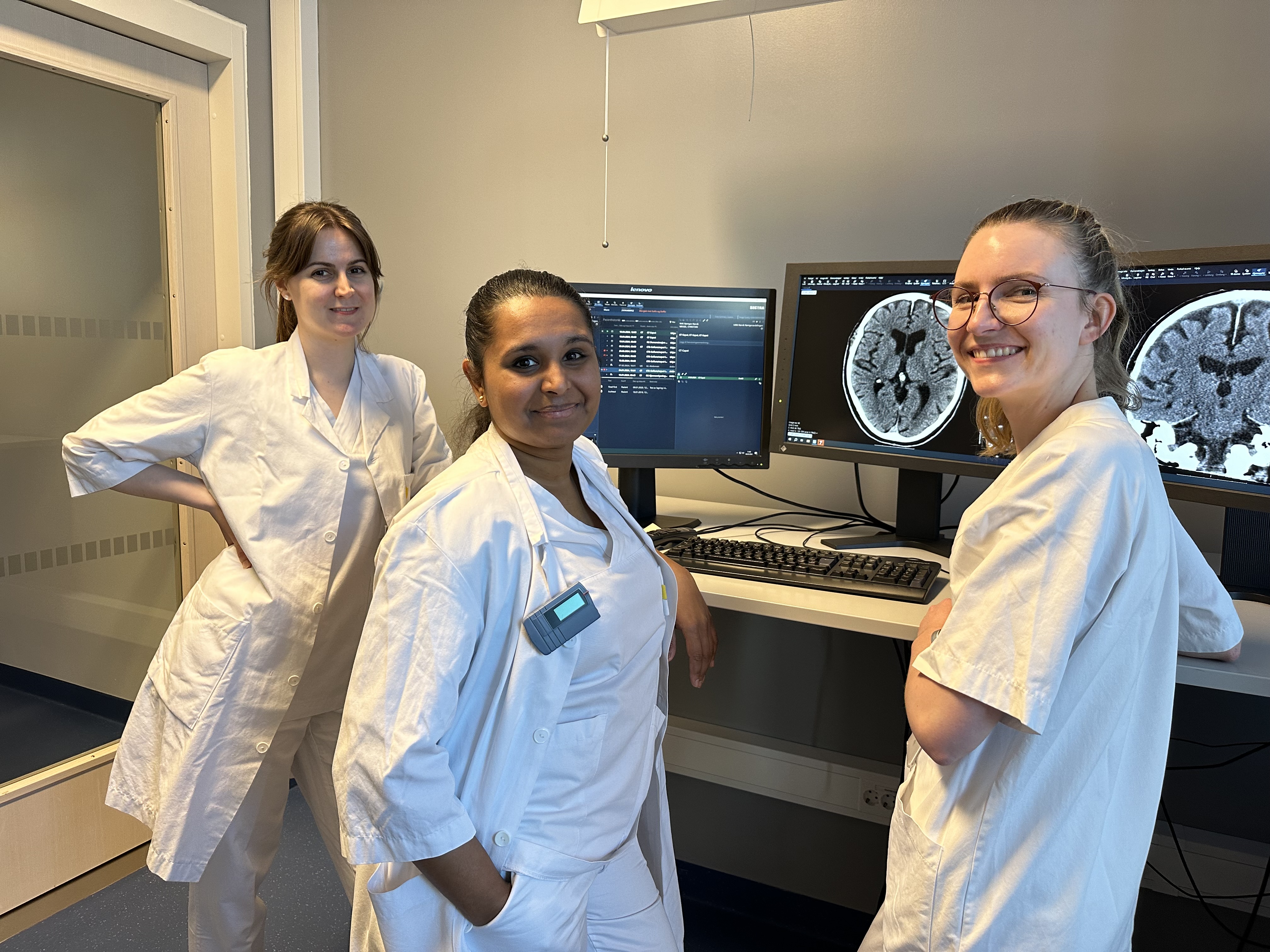 En gruppe kvinner i hvite labfrakker står foran en datamaskin