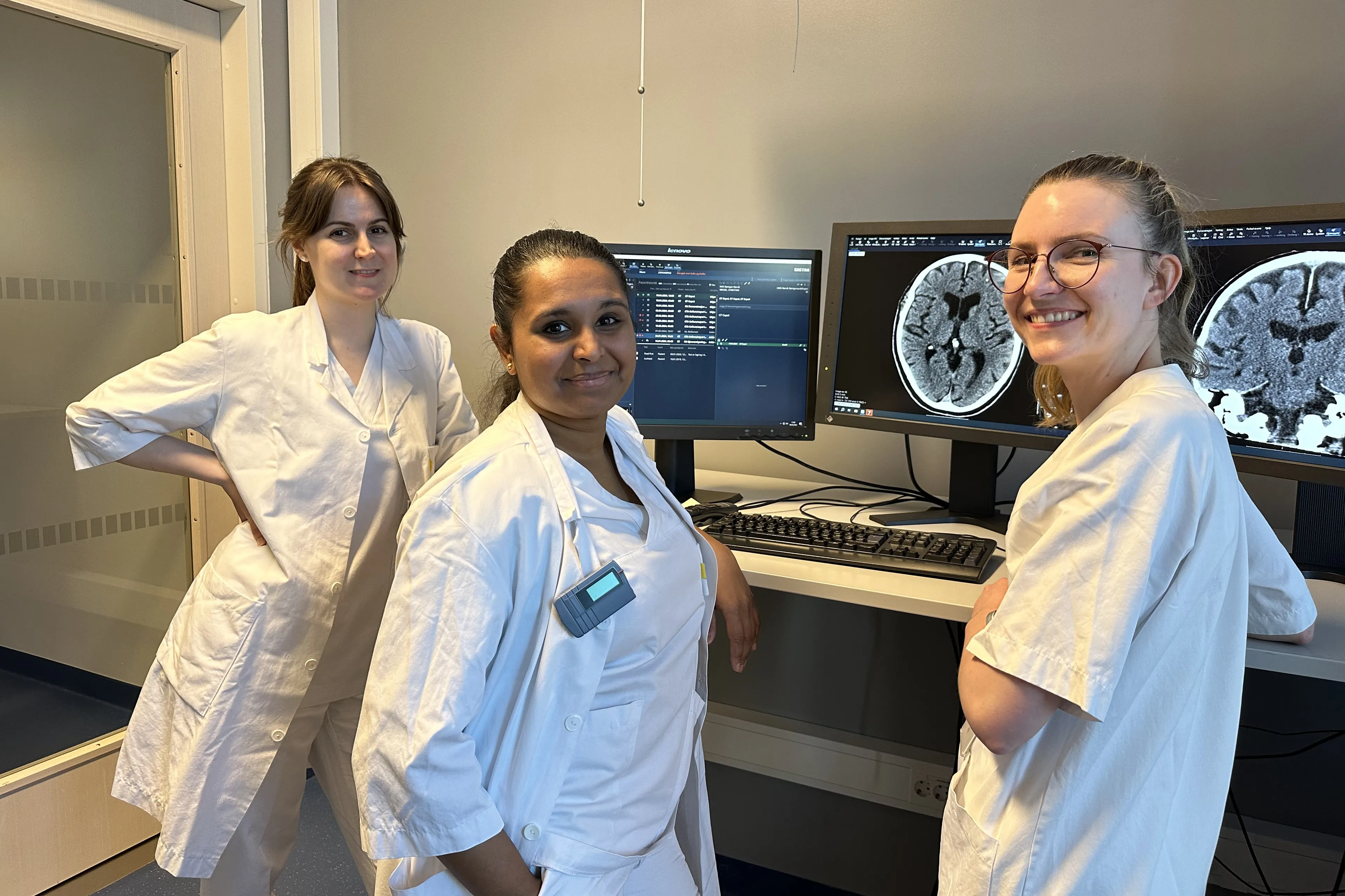 En gruppe kvinner i hvite labfrakker står foran en datamaskin