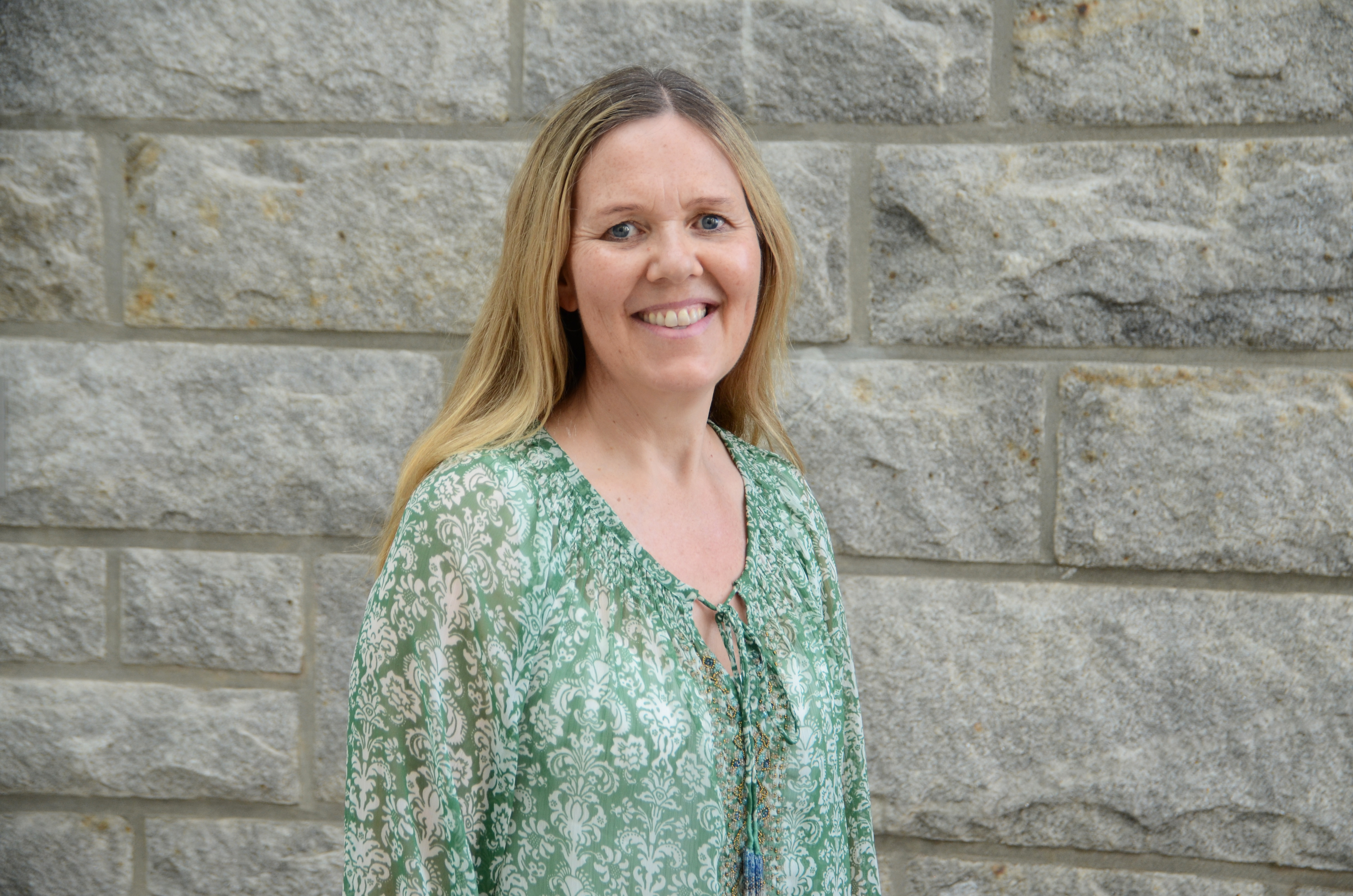 En kvinne som smiler foran en steinmur