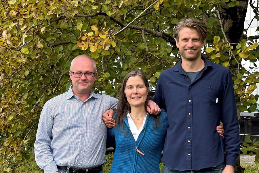 To menn og en dame som står samlet foran et tre