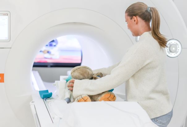 En dame som sitter atmed en bamse som ligger på en seng