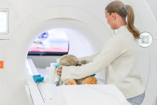 En dame som sitter atmed en bamse som ligger på en seng
