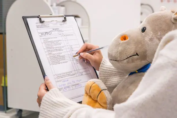 Dame som sitter med bamse på fanget og skriver på et arkl