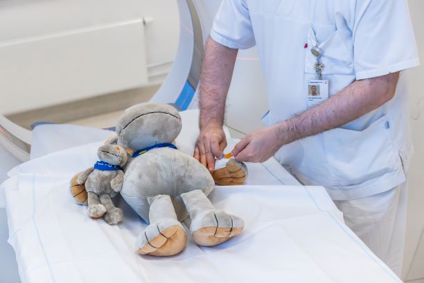En bamse som ligger på ei seng og får hjelp av en sykepleier