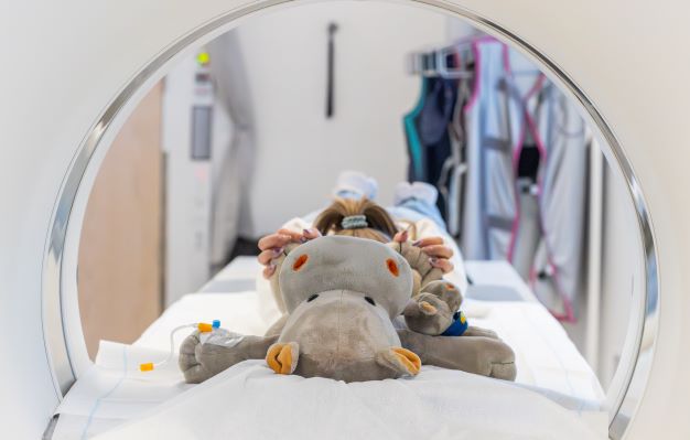 En bamse som ligger på en seng som er inni en røntgenmaskin