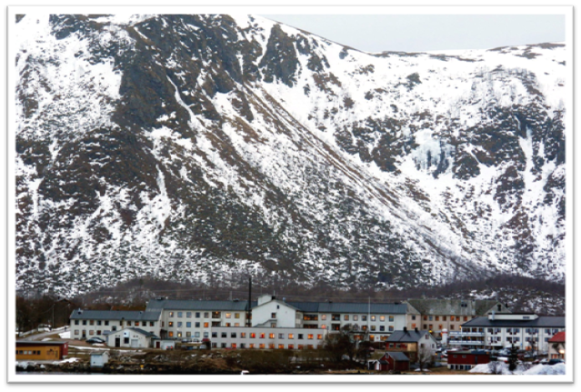 Stort hvitt bygg foran et fjell med snø
