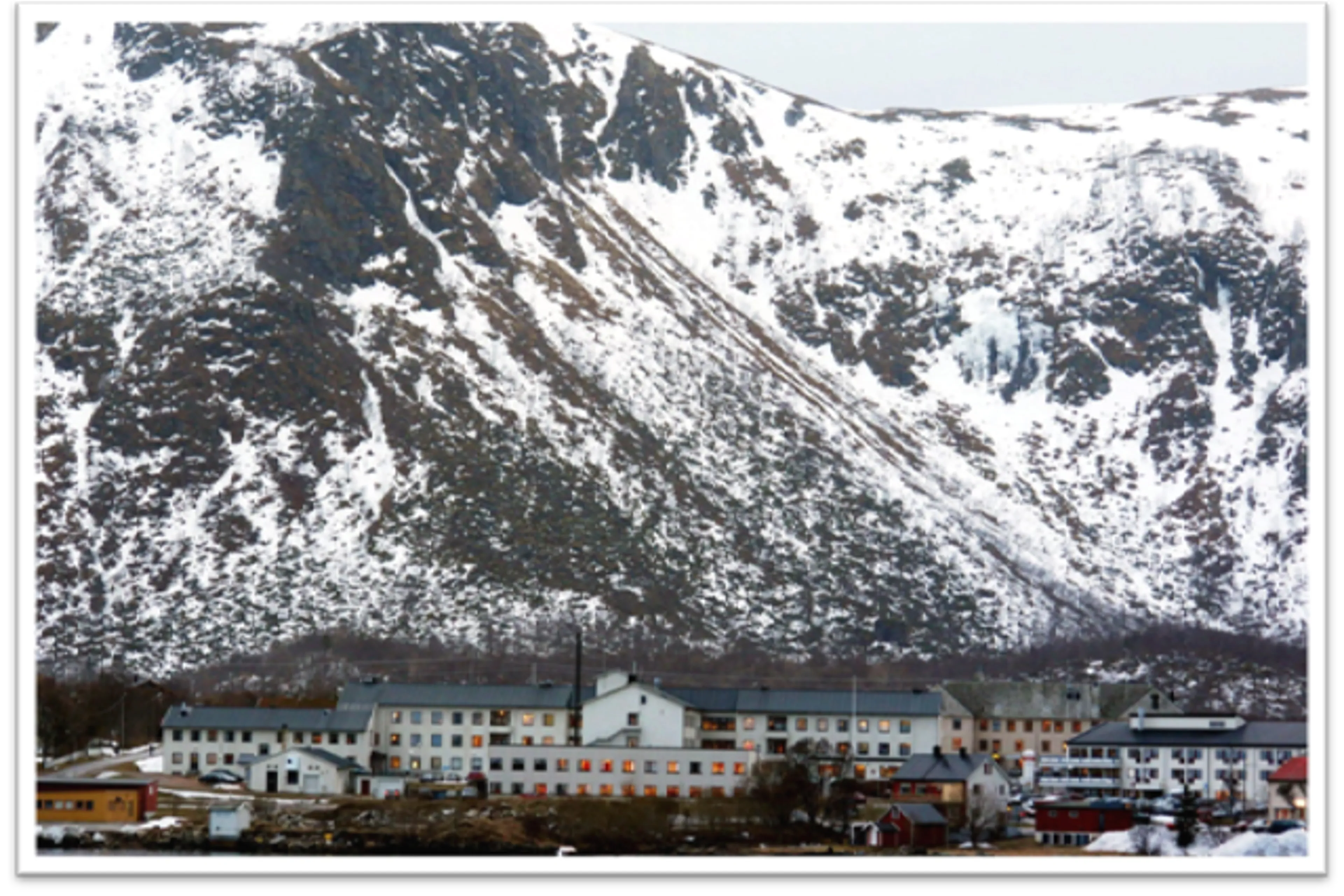 Stort hvitt bygg foran et fjell med snø