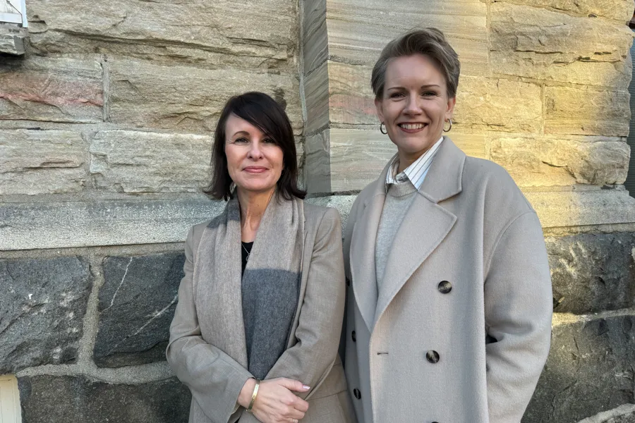 To damer som står foran en marmorvegg og smiler