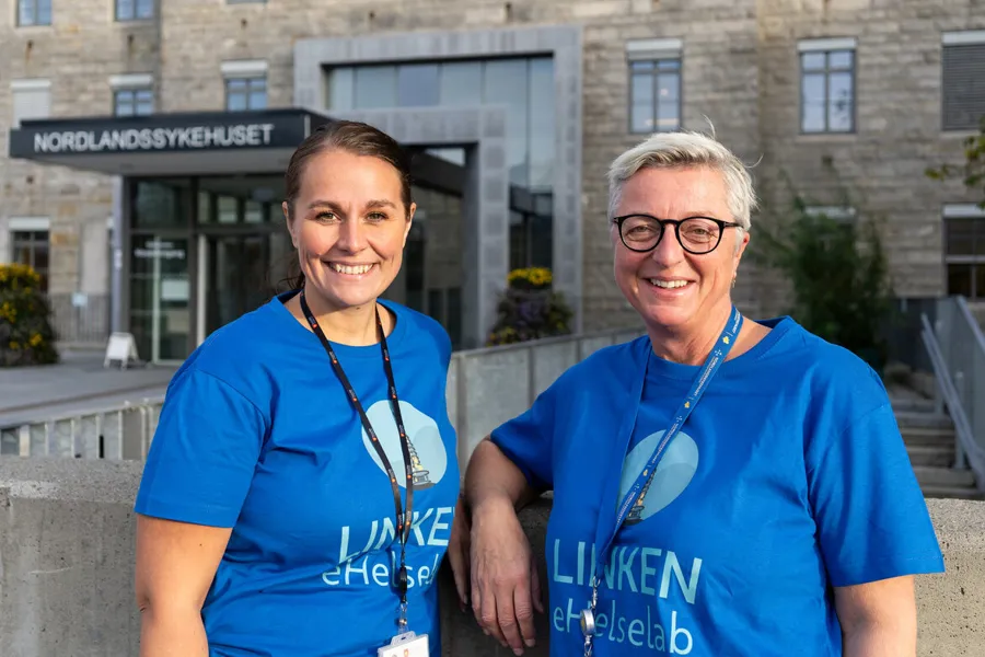 To damer som står foran et sykehusbygg og smiler