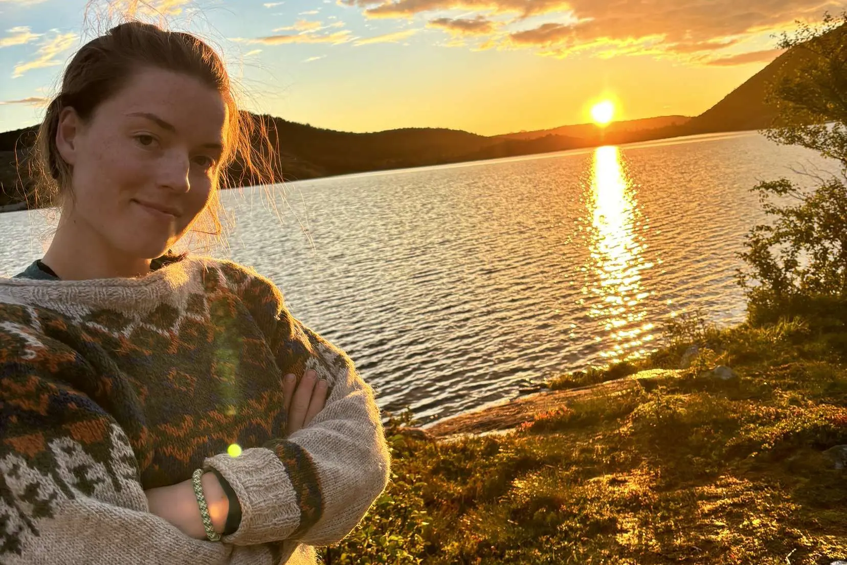 En person som står ved en vannmasse med en solnedgang i bakgrunnen