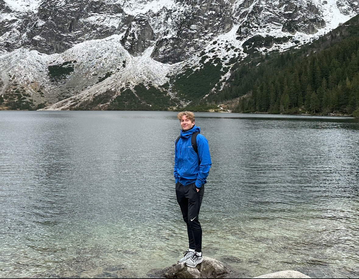 En mann som står på en stein ved en innsjø med et fjell i bakgrunnen