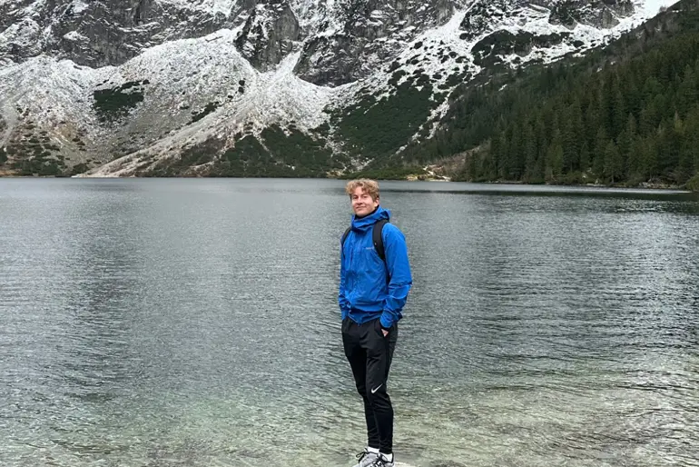 En mann som står på en stein ved en innsjø med et fjell i bakgrunnen