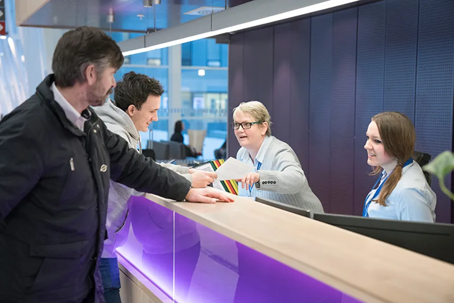 To menn som snakker med to damer over en skranke