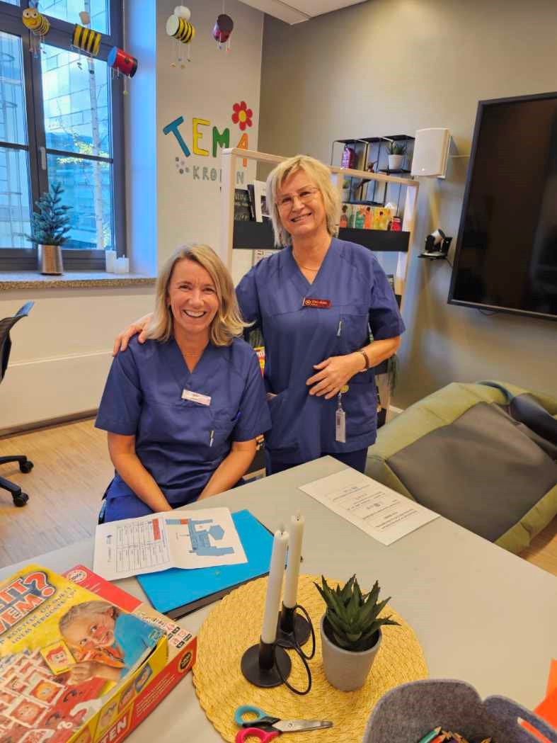 Et par kvinner som står ved siden av et bord med bøker og en plante