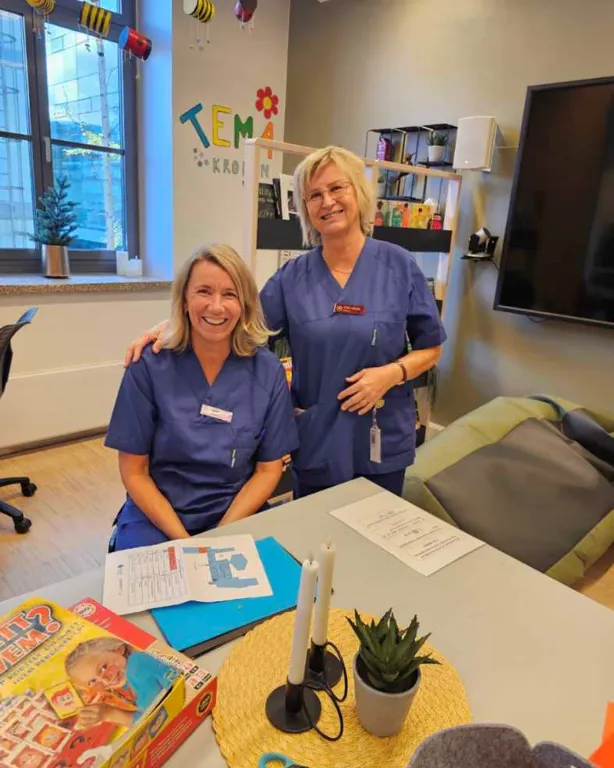 Et par kvinner som står ved siden av et bord med bøker og en plante