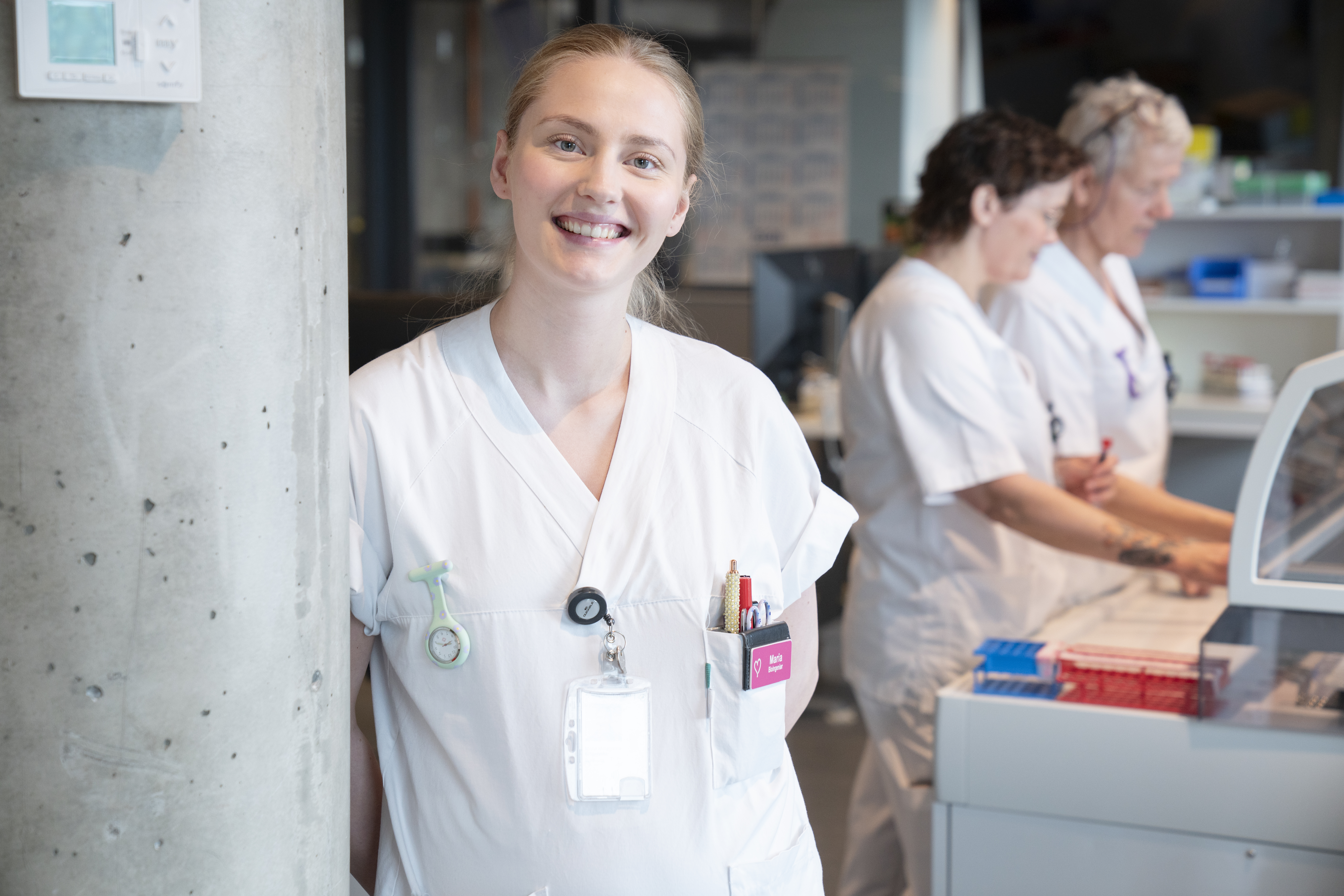 Dame som står i hvite sykehusklær og smiler
