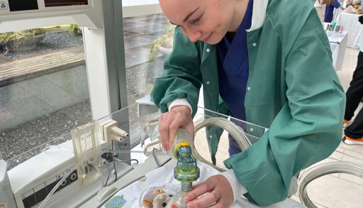 A person in a lab coat looking at a small animal in a tube