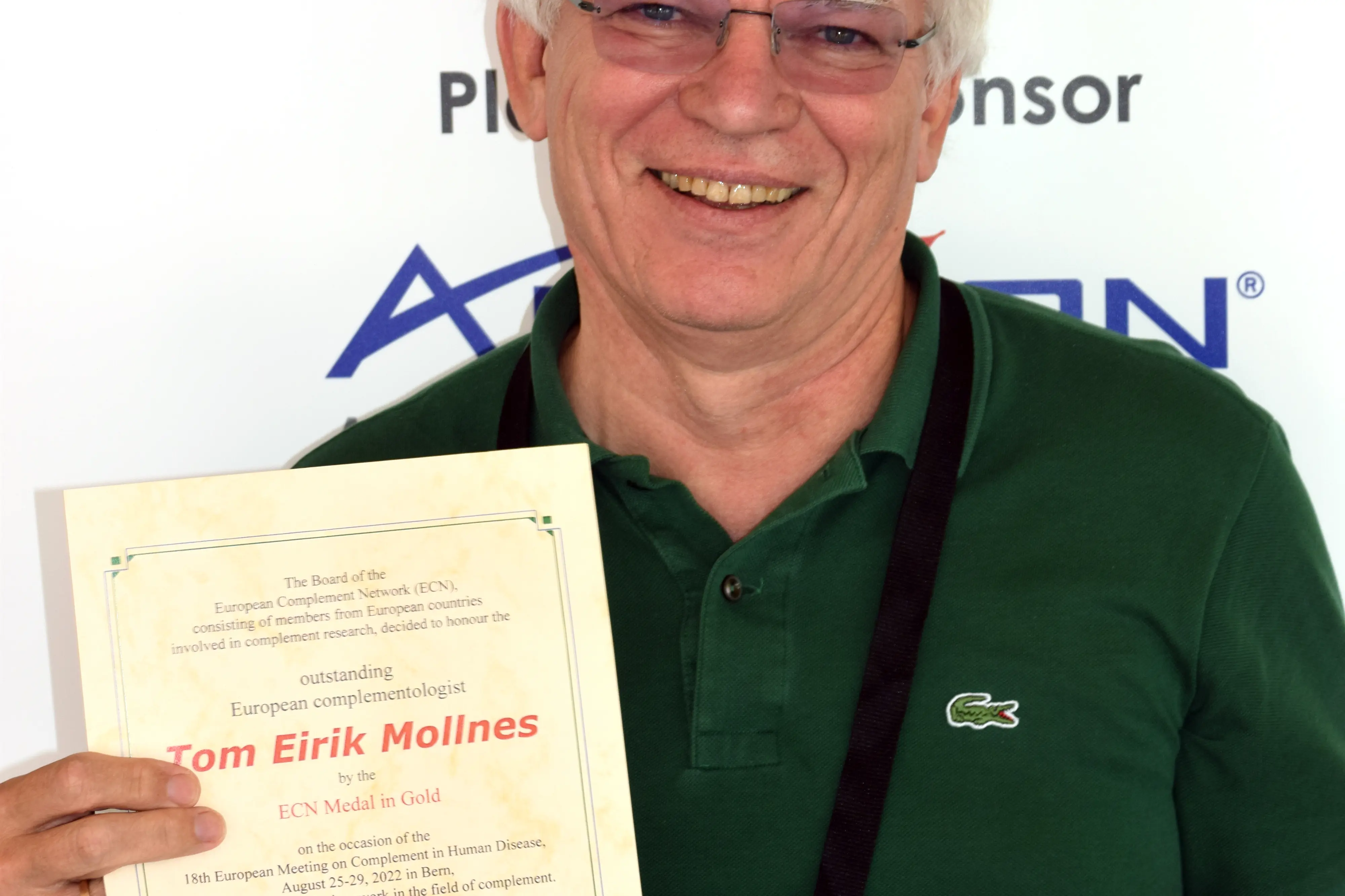 Mann som smiler mot kamera og holder diplom og medalje