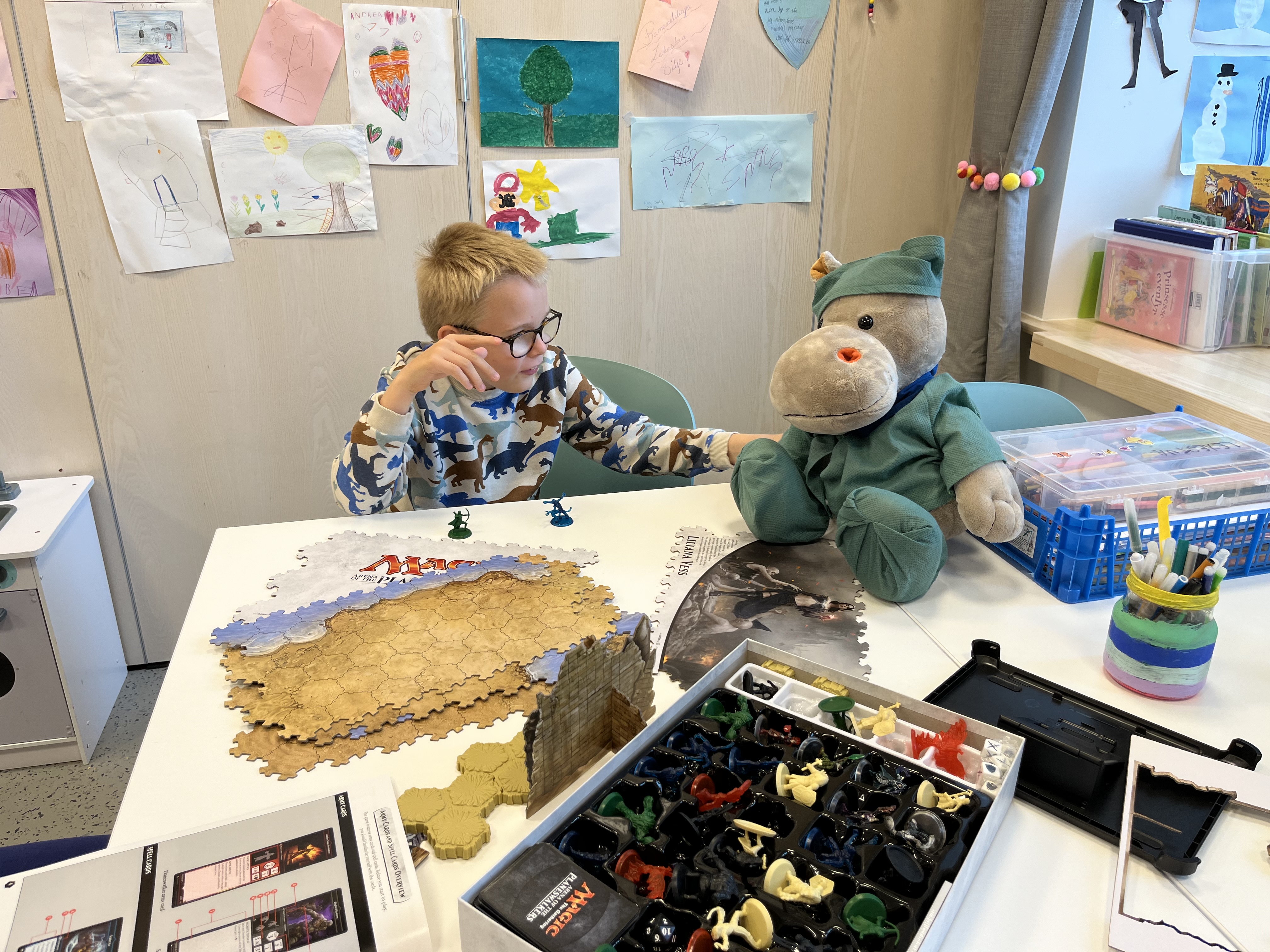 Gutt som sitter ved bord å ser på bamse ikledd sykehusklær