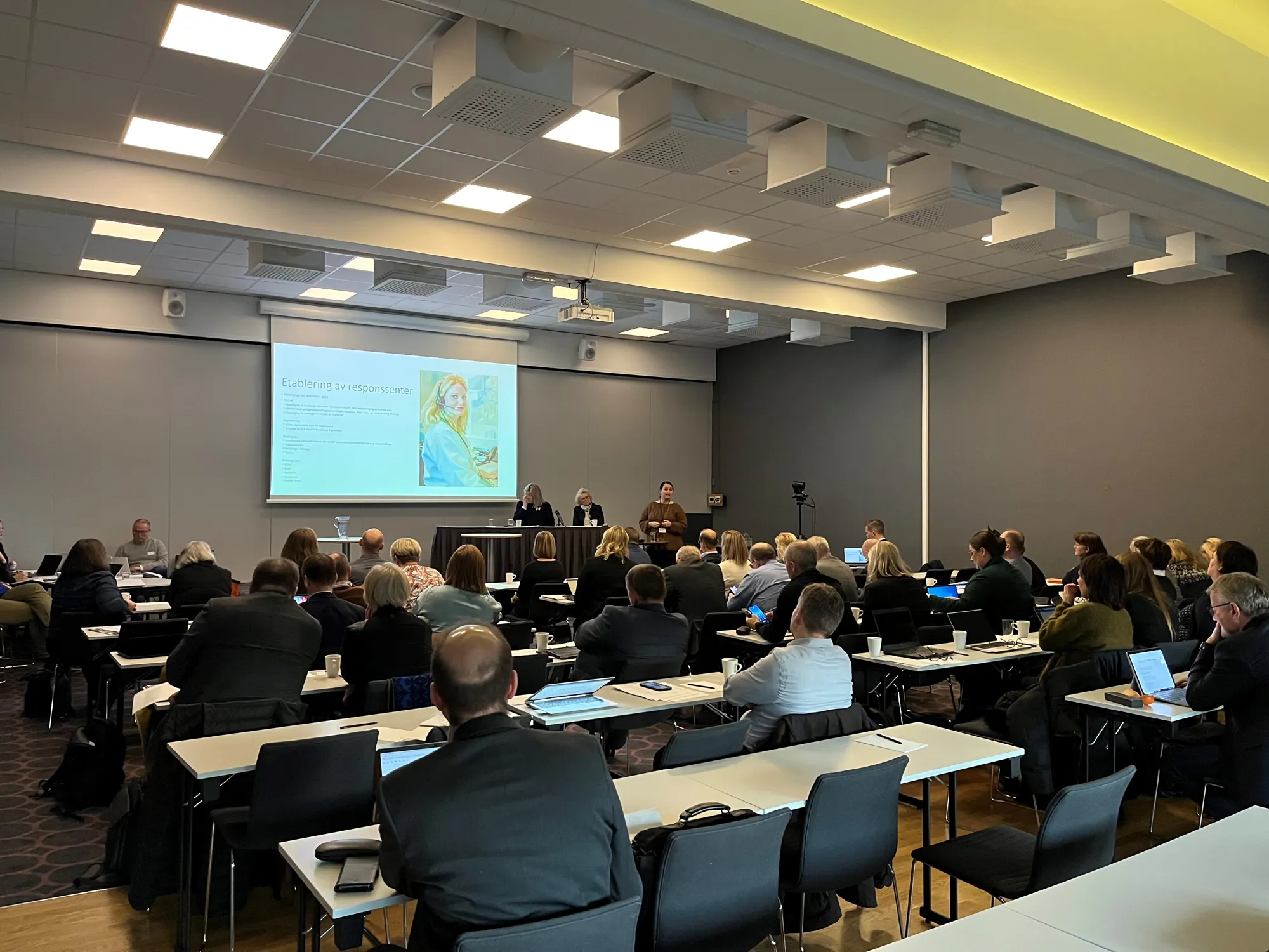 Konferanserom med deltakere som følger med på en presentasjon