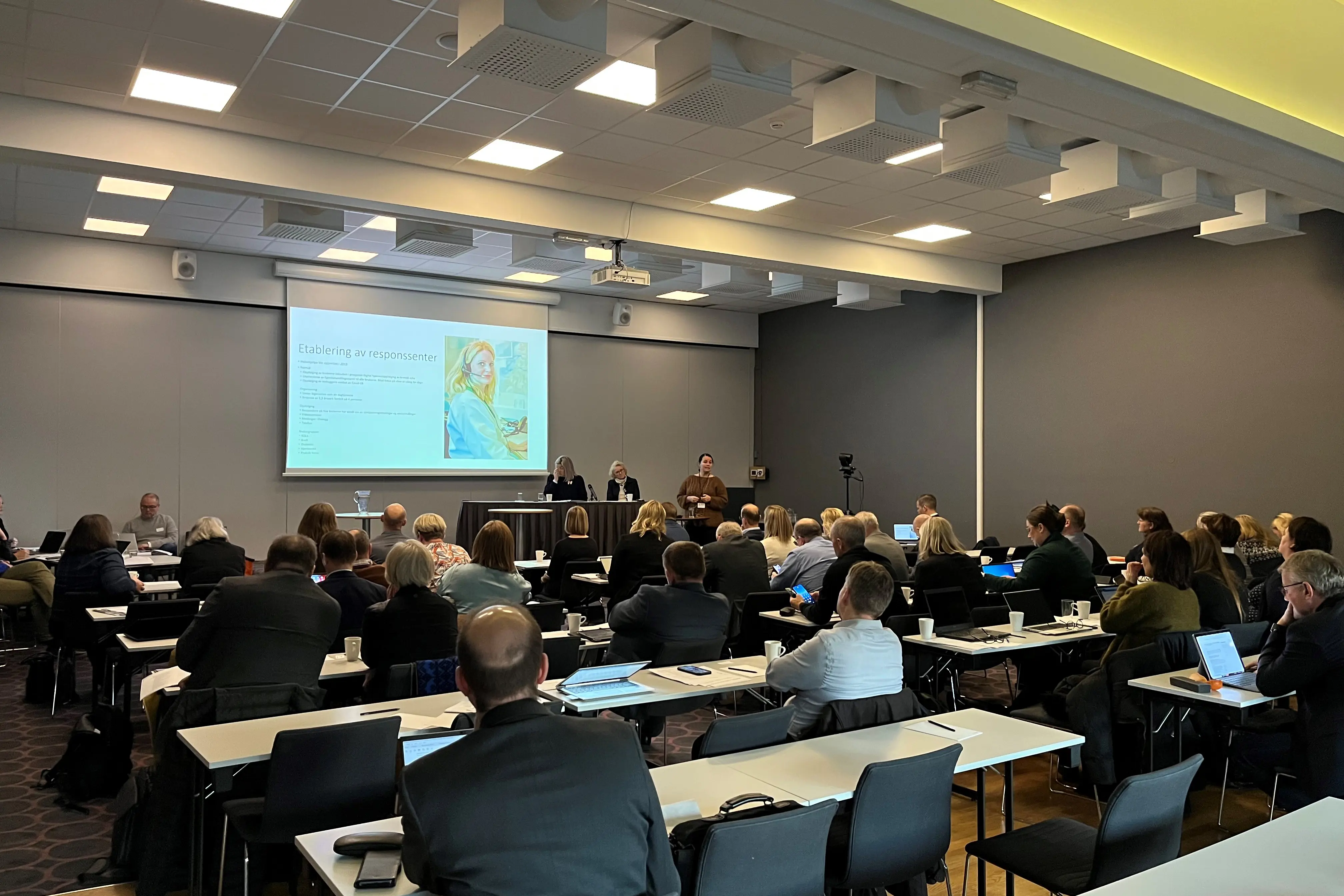 Konferanserom med deltakere som følger med på en presentasjon