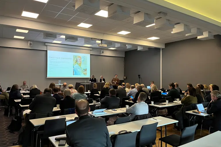 Konferanserom med deltakere som følger med på en presentasjon
