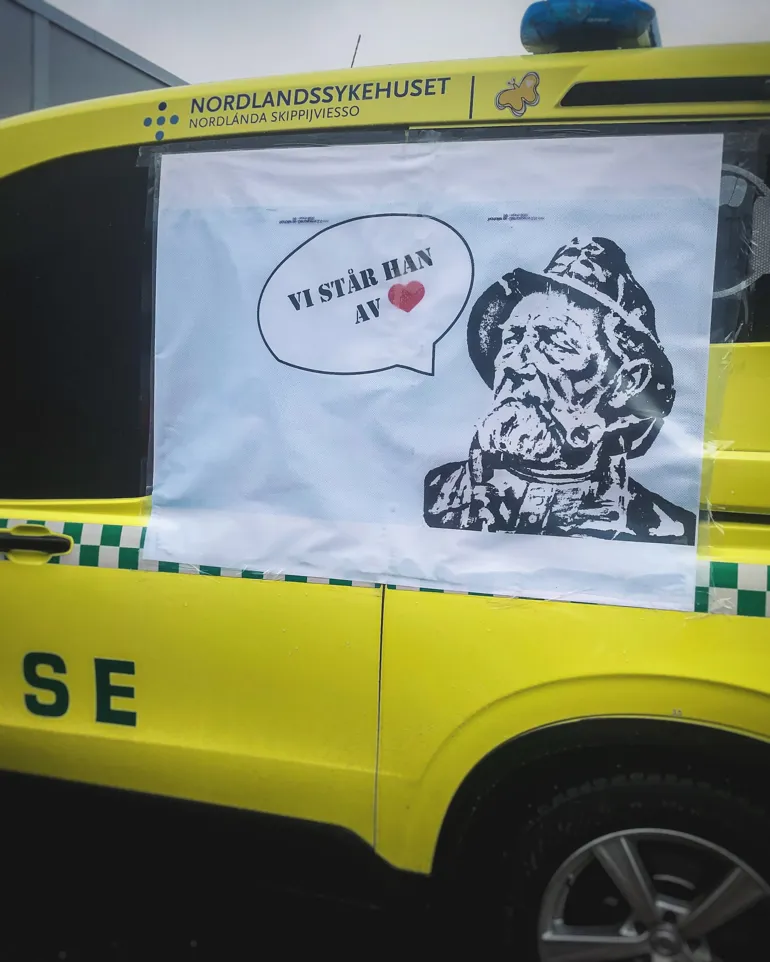 Ambulanse med plakat med teksten "Vi står han av"