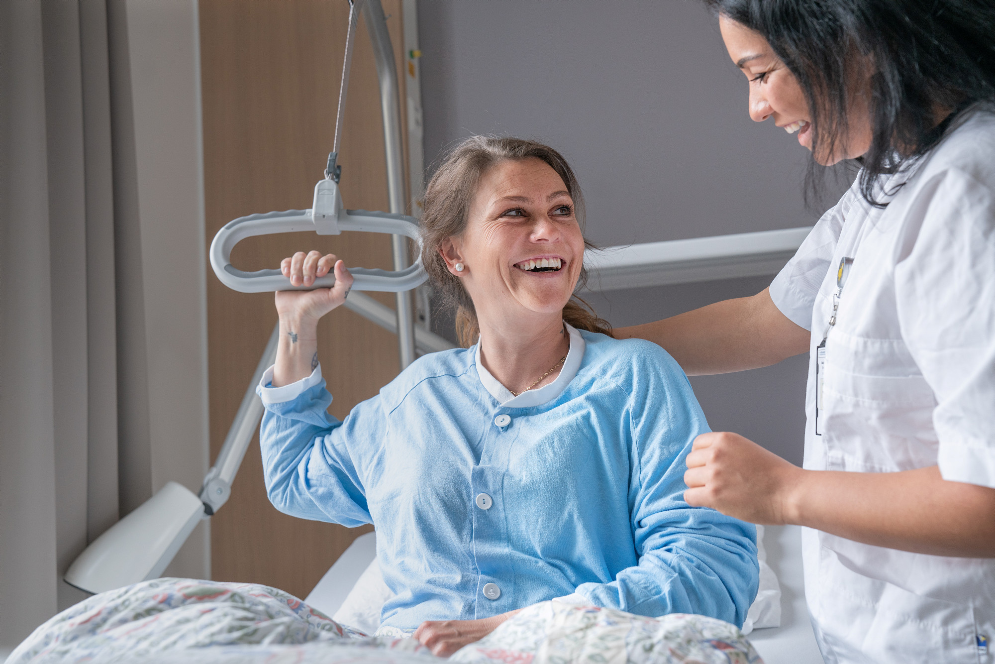 Pasient som ligger i seng og smiler til sykepleier