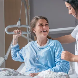 Pasient som ligger i seng og smiler til sykepleier