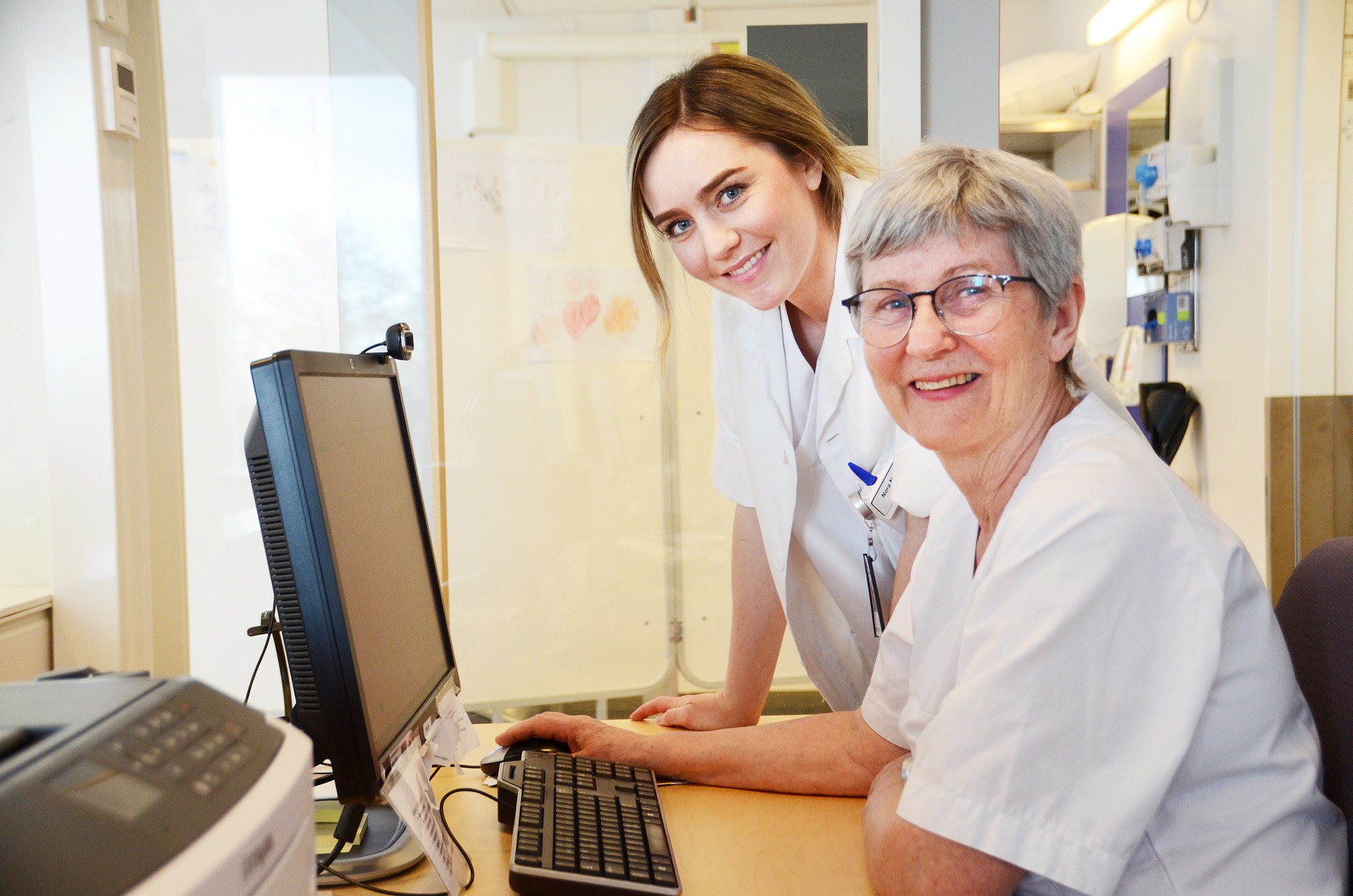 To damer ved PC som ser mot kamera og smiler