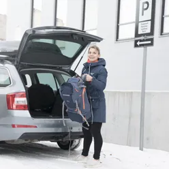 Dame som holder i en ryggsekk som skal legges inn i bagasjerommet på en bil