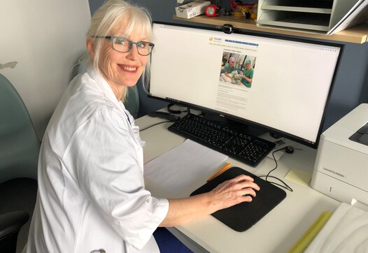 Lege som sitter ved PC og smiler mot kamera