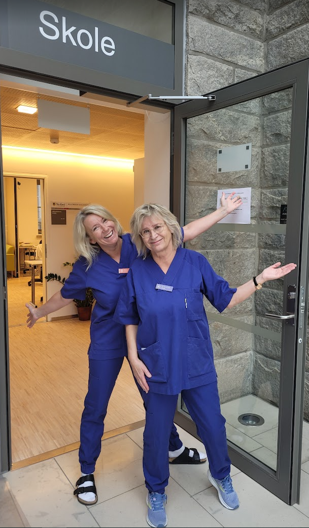 To damer i blå klær som smiler til kamera